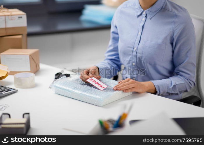 delivery, mail service, and shipment concept - close up of woman sticking fragile mark to parcel in protective bubble wrap at post office. woman sticking fragile mark to wrap at post office