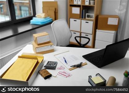 delivery, mail service and shipment concept - laptop, clipboard, parcel boxes and packing stuff on table at post office. laptop and parcels on table at post office