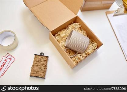 delivery, mail service and shipment concept - parcel box with straw filler and mug at post office. parcel with straw filler and mug at post office