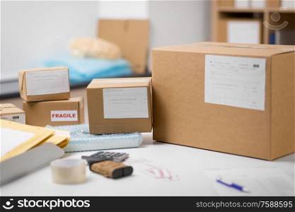 delivery, mail service and shipment concept - parcel boxes and packing stuff on table at post office. parcel boxes and packing stuff at post office