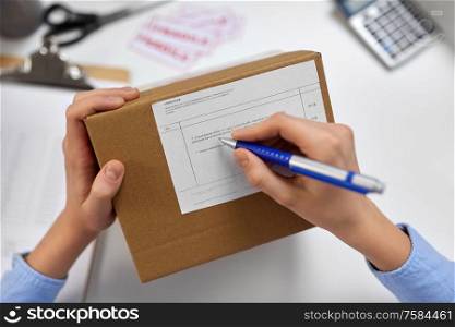 delivery, mail service, people and shipment concept - close up of female hands filling postal form on parcel box at office. close up of hands filling form on parcel at office