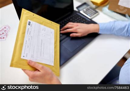 delivery, mail service, people and shipment concept - close up of female hands with laptop computer and envelope parcel with postal form on it at post office. hands with laptop and envelope at post office