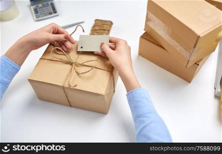 delivery, mail service, people and shipment concept - close up of female hands tying name tag to parcel box at post office. hands tying name tag to parcel box at post office