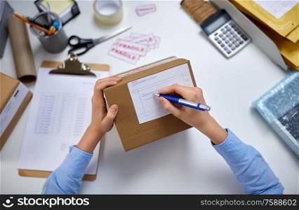 delivery, mail service, people and shipment concept - close up of female hands filling postal form on parcel box at office. close up of hands filling form on parcel at office