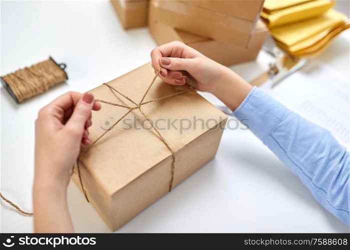 delivery, mail service, people and shipment concept - close up of female hands packing eco parcel box and tying rope at post office. hands packing parcel and tying rope at post office