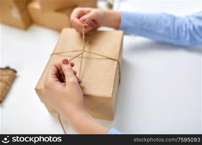 delivery, mail service, people and shipment concept - close up of female hands packing eco parcel box and tying rope at post office. hands packing parcel and tying rope at post office
