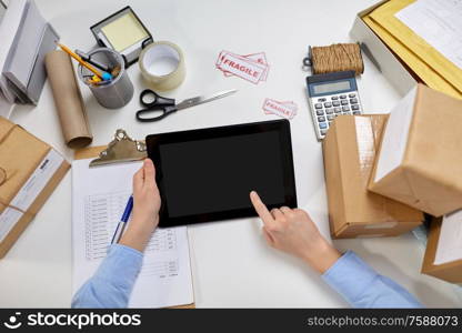 delivery, mail service, people and shipment concept - close up of hands with tablet pc computer, parcel boxes and form on clipboard at post office. hands with tablet pc and clipboard at post office