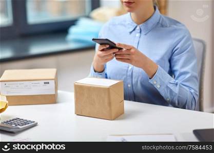 delivery, mail service, people and shipment concept - close up of woman with smartphone and parcel boxes at post office. woman with smartphone and parcels at post office