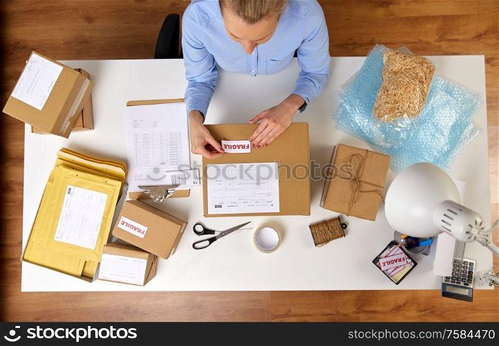 delivery, mail service, people and shipment concept - close up of woman sticking fragile mark to parcel box at post office. woman sticking fragile mark to parcel box