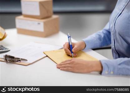 delivery, mail service, people and shipment concept - close up of woman with pen writing address on parcel envelope at post office. woman writing on parcel envelope at post office