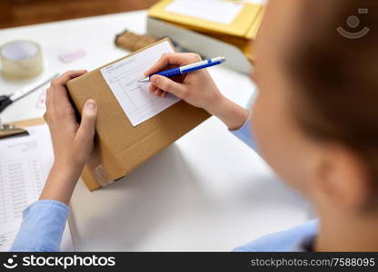 delivery, mail service, people and shipment concept - close up of woman filling postal form on parcel box at office. close up of woman filling postal form at office