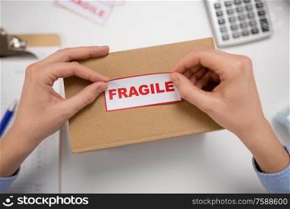 delivery, mail service, people and shipment concept - close up of woman sticking fragile mark to parcel box at post office. woman sticking fragile mark to parcel box