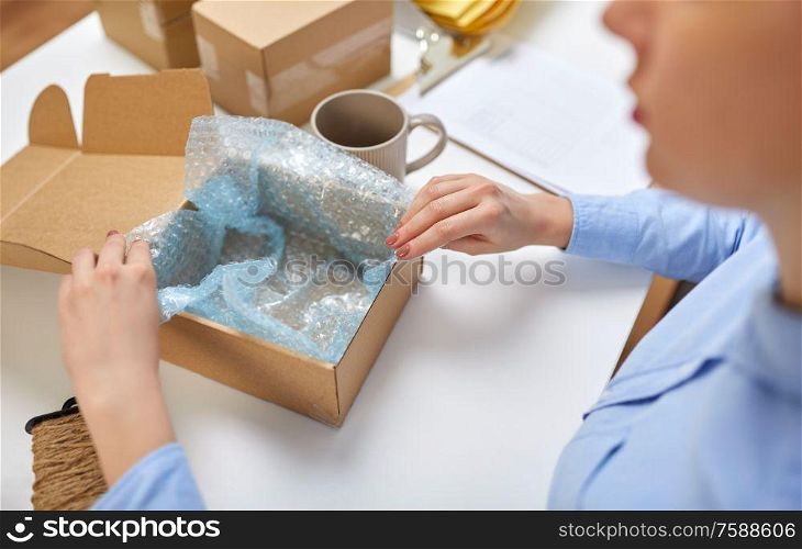 delivery, mail service, people and shipment concept - close up of woman packing mug into parcel box and it wrapping into protective bubble wrap at post office. woman packing mug to parcel box at post office