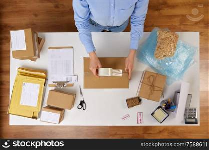 delivery, mail service, people and shipment concept - close up of woman packing parcel box with adhesive tape at post office. woman packing parcel box with adhesive tape