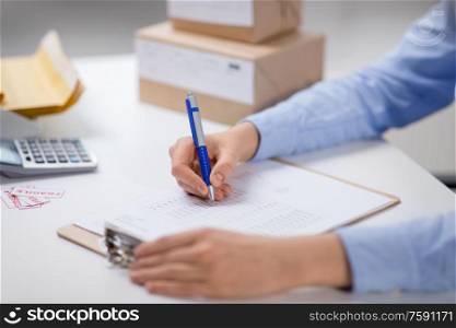 delivery, mail service, people and shipment concept - close up of woman with clipboard filling checklist at post office. woman with clipboard and parcels at post office