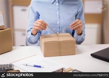 delivery, mail service, people and shipment concept - close up of woman packing parcel box and tying rope at post office. woman packing parcel and tying rope at post office