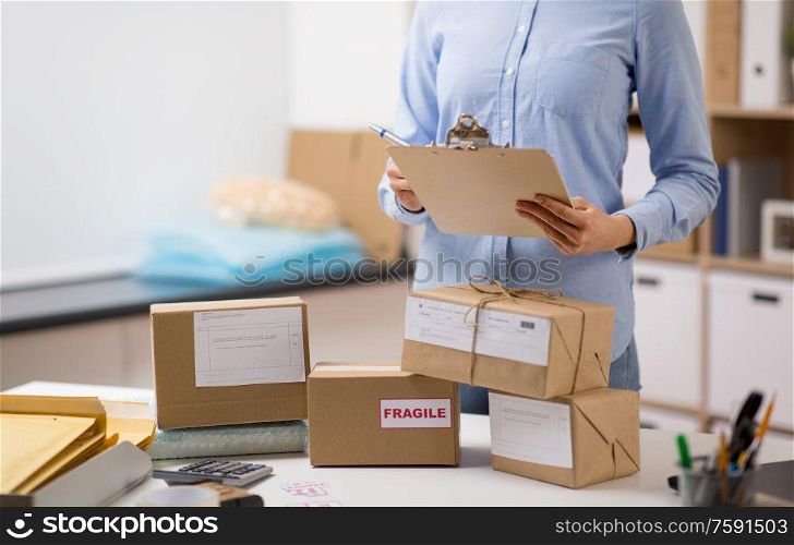 delivery, mail service, people and shipment concept - close up of woman with parcel boxes and clipboard working at post office. woman with parcels and clipboard at post office