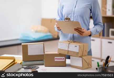 delivery, mail service, people and shipment concept - close up of woman with parcel boxes and clipboard working at post office. woman with parcels and clipboard at post office