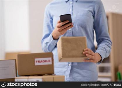 delivery, mail service, people and shipment concept - close up of woman with smartphone and parcel boxes at post office. woman with smartphone and parcels at post office