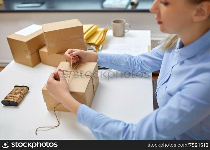 delivery, mail service, people and shipment concept - close up of woman packing eco parcel box and tying rope at post office. woman packing parcel and tying rope at post office