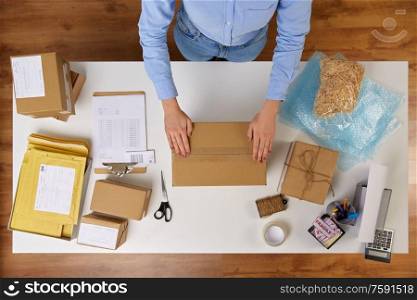 delivery, mail service, people and shipment concept - close up of woman packing parcel box with adhesive tape at post office. woman packing parcel box with adhesive tape
