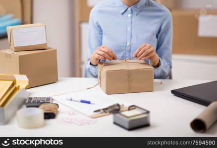 delivery, mail service, people and shipment concept - close up of woman packing parcel box and tying rope at post office. woman packing parcel and tying rope at post office