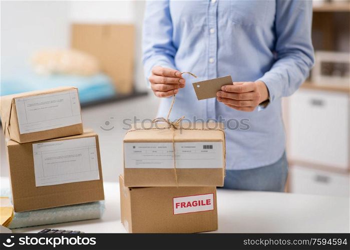 delivery, mail service, people and shipment concept - close up of woman packing parcel box and tying tag by rope at post office. woman packing parcel and tying tag at post office