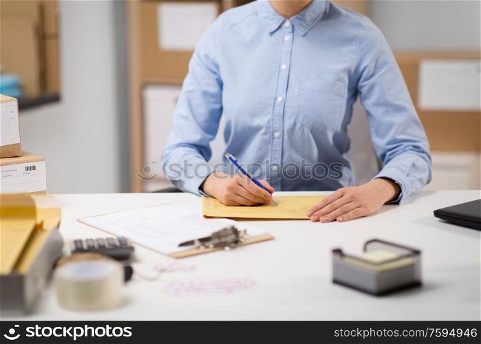 delivery, mail service, people and shipment concept - close up of woman with pen writing address on parcel envelope at post office. woman writing on parcel envelope at post office