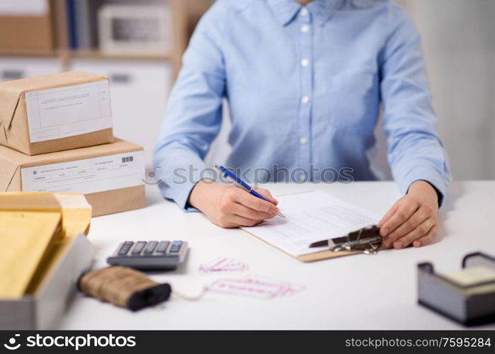 delivery, mail service, people and shipment concept - close up of woman with clipboard filling checklist at post office. woman with clipboard and parcels at post office