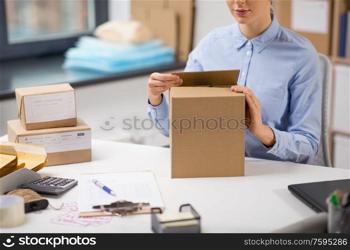 delivery, mail service, people and shipment concept - close up of woman packing parcel box at post office. woman packing parcel box at post office