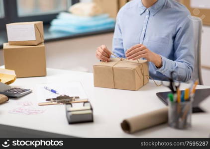 delivery, mail service, people and shipment concept - close up of woman packing parcel box and tying rope at post office. woman packing parcel and tying rope at post office