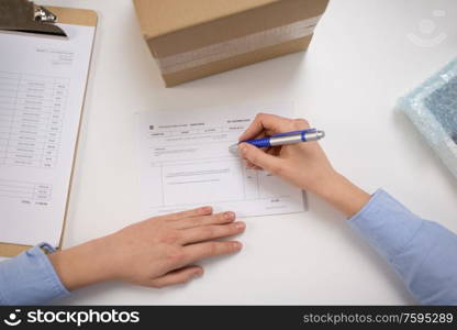 delivery, mail service, people and shipment concept - close up of woman filling postal form at office. close up of woman filling postal form at office