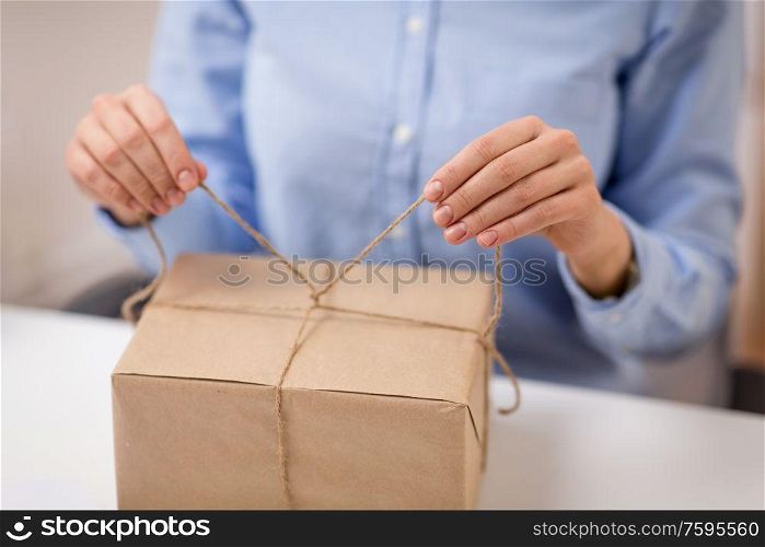 delivery, mail service, people and shipment concept - close up of woman packing parcel or gift box and tying rope. woman packing parcel or gift box and tying rope
