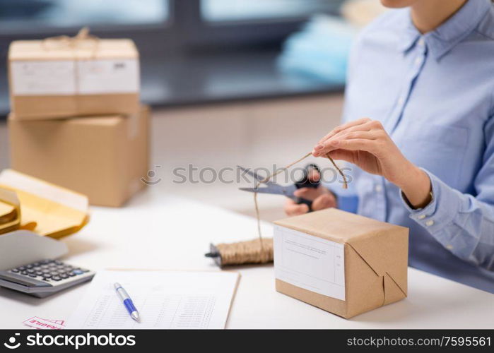 delivery, mail service, people and shipment concept - close up of woman packing parcel box and cutting rope with scissors at post office. woman with parcel cutting rope at post office