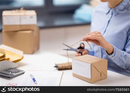 delivery, mail service, people and shipment concept - close up of woman packing parcel box and cutting rope with scissors at post office. woman with parcel cutting rope at post office