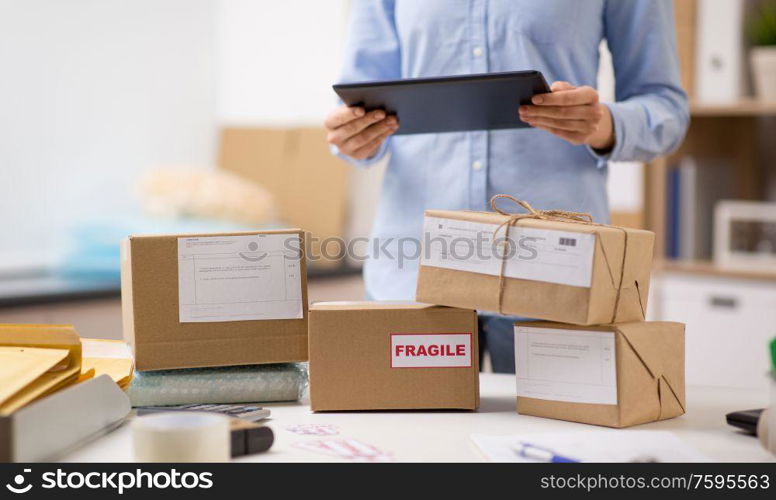 delivery, mail service, people and shipment concept - close up of woman with tablet pc computer and parcel boxes at post office. woman with tablet pc and parcels at post office