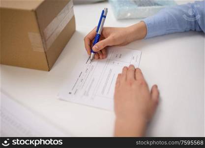 delivery, mail service, people and shipment concept - close up of woman filling postal form at office. close up of woman filling postal form at office