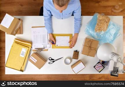 delivery, mail service, people and shipment concept - close up of woman filling postal form on envelope parcel box at office. close up of woman filling postal form at office