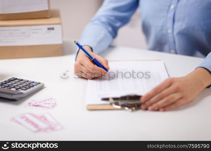 delivery, mail service, people and shipment concept - close up of woman with clipboard filling checklist at post office. woman with clipboard and parcels at post office