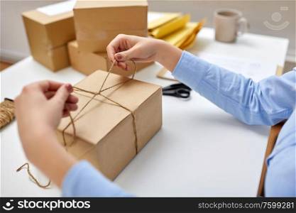 delivery, mail service, people and shipment concept - close up of woman packing eco parcel box and tying rope at post office. woman packing parcel and tying rope at post office