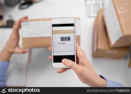 delivery, mail service, people and shipment concept - close up of woman&rsquo;s hands with smartphone scanning barcode on parcel box at post office. hands with smartphone scans barcode on parcel box