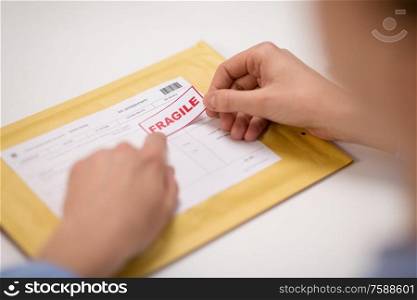 delivery, mail service, people and shipment concept - close up of woman&rsquo;s hands sticking fragile marks to parcel in envelope at post office. hands sticking fragile marks to parcel in envelope