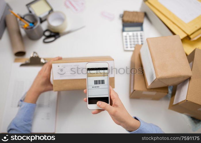 delivery, mail service, people and shipment concept - close up of woman&rsquo;s hads with smartphone scanning barcode on parcel box at post office. hands with smartphone scans barcode on parcel box