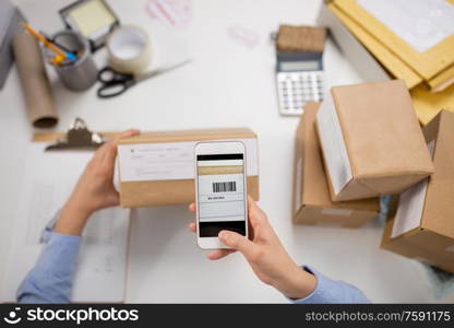 delivery, mail service, people and shipment concept - close up of woman&rsquo;s hads with smartphone scanning barcode on parcel box at post office. hands with smartphone scans barcode on parcel box