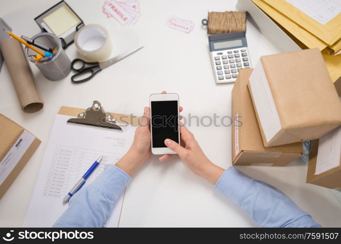 delivery, mail service, people and shipment concept - close up of woman&rsquo;s hands with smartphone and parcel boxes at post office. hands with smartphone and parcels at post office