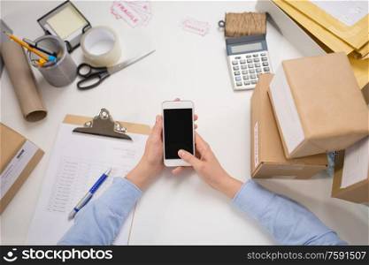 delivery, mail service, people and shipment concept - close up of woman&rsquo;s hands with smartphone and parcel boxes at post office. hands with smartphone and parcels at post office