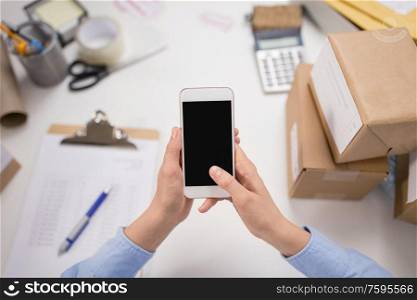 delivery, mail service, people and shipment concept - close up of woman&rsquo;s hands with smartphone and parcel boxes at post office. hands with smartphone and parcels at post office