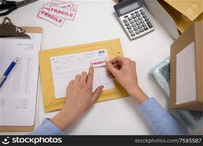 delivery, mail service, people and shipment concept - close up of woman&rsquo;s hands sticking fragile marks to parcel in envelope at post office. hands sticking fragile marks to parcel in envelope