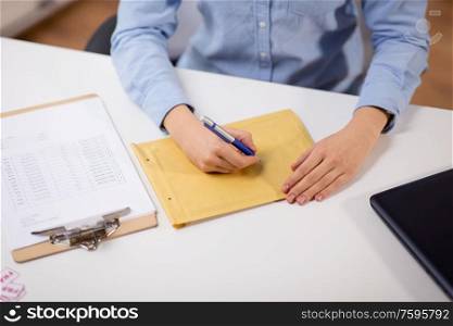 delivery, mail service, people and shipment concept - close up of woman&rsquo;s hands with pen writing address on parcel envelope at post office. woman writing on parcel envelope at post office