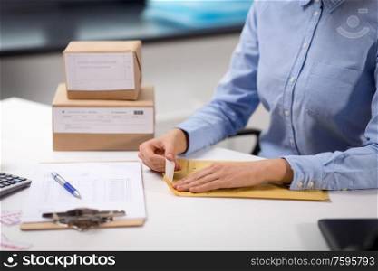 delivery, mail service, people and shipment concept - close up of woman&rsquo;s hands removing sticker from envelope with parcel at post office. woman removing sticker from envelope with parcel